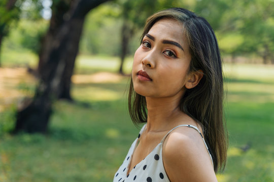 Close-up of unhappy Southeast Asian woman with tears looking at camera in outdoor park. Portrait of depressed and stressful girl crying in summer - head shot