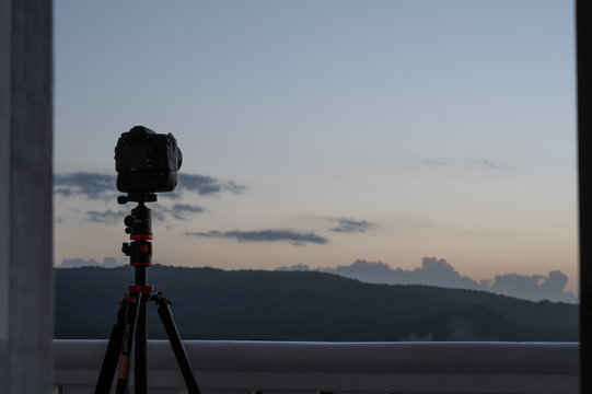 a dslr camera on a tripod is silhouetted against a sunset sky from a balcony as it takes a time-lapse set of pictures