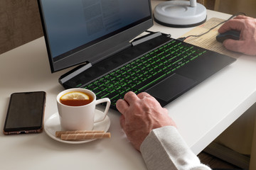 A man works on a computer at home. Remote work, social distancing, quarantine concept. Selective focus. Horizontal orientation.