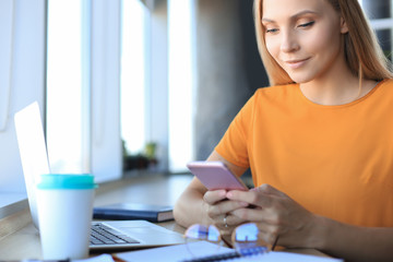 Beautiful business woman is using her smartphone with smile while sitting at her working place