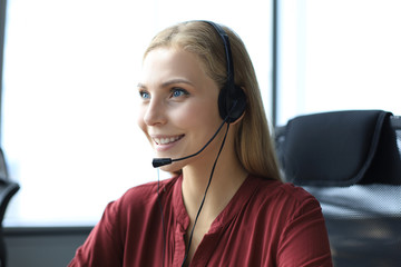 Beautiful smiling call center worker in headphones is working at modern office