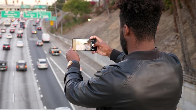 African-American man takes photos of the morning traffic with his smartphone in Los Angeles