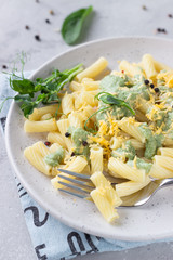 Penne pasta with green cream sauce, cheese and micro greens on a ceramic plate, light grey stone background. Italian food. 