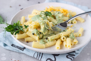 Penne pasta with green cream sauce, cheese and micro greens on a ceramic plate, light grey stone background. Italian food. Close up.