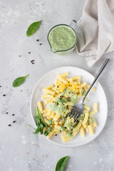 Penne pasta with green cream sauce, cheese and micro greens on a ceramic plate, light grey stone background. Italian food. Top view. 