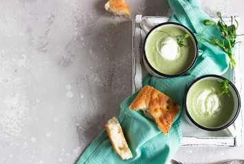 Healthy broccoli soup with cream in enameled mugs with fresh focaccia and micro greens served in a...