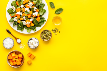 Salad with pumpkin and basil - near ingredients - on yellow background top-down copy space