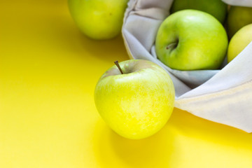 Reusable cotton textile bag with green apples on a yellow paper background. The concept of zero waste, ecology shopping. 