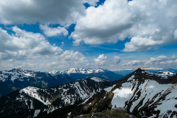 A distant view on the snowy slopes of Austrian Alps. There is a massive mountain chain in the back, partially covered with snow. Early spring coming to the Alps. Overcast. Achievement and fun.