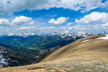 Obraz premium A vast view on Alpine valley from the upper parts of Himmeleck in Austria. The valley is lush green. There are many mountain ranges in the back, covered with snow. Spring coming to the Alps.