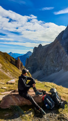A man in hiking outfit resting and enjoying the view on Austrian Alps in autumn. There is massive, rocky mountain behind him. New day beginning. Contemplation and meditation. Calm state of mind.