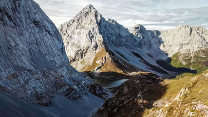 A drone shot of Alpine landscape of Wolayer Lake in Austria. Sharp slopes of both side of the valley. Hard to reach mountain peaks. There are many mountain ranges in the back. Serenity and calmness