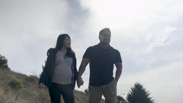 Young Pregnant Couple Holding Hands, Walk on Path on Hill, Grey Sky SLOW MOTION