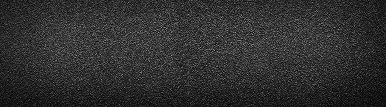 Ultra wide rough black surface. Panoramic background with darkened edges. Texture of flat and grainy sandpaper or panorama of uneven wall material.