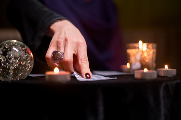 Fototapeta na wymiar Close-up of fortune teller woman divining on cards sitting at table with burning candles, magic ball