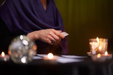 Fortune teller female in purple dress divines on cards sitting at table with candles