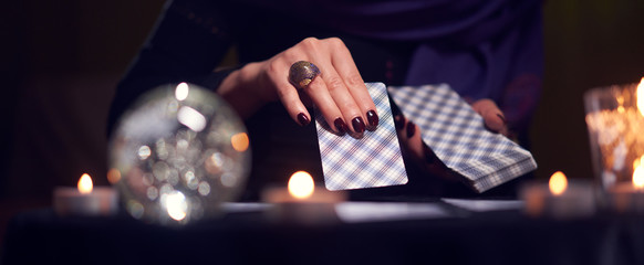 Close-up of fortuneteller's hands with cards at table with candles, magic ball in dark room - obrazy, fototapety, plakaty