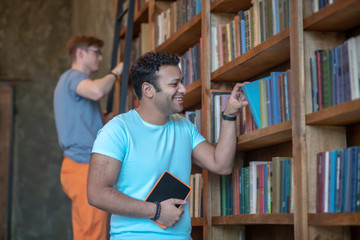 Two friends looking for the needed books for preparation to exams and smiling