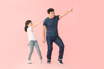 Happy Asian man and his little daughter dancing against color background