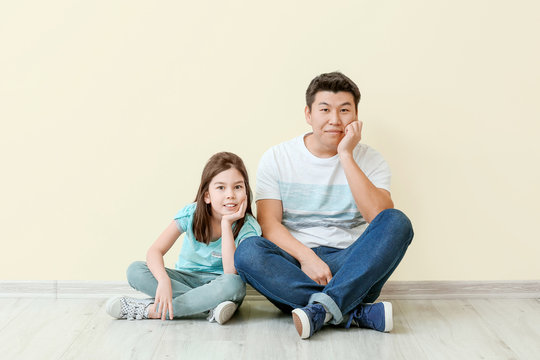 Happy Asian man and his little daughter sitting near color wall