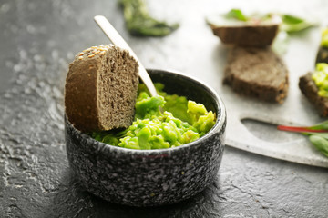 Bowl with blended avocado and bread on dark background