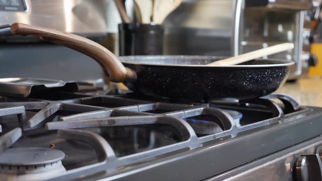 Pan down focus of cooking pan on stove, blurred background of toaster and cooking utensils