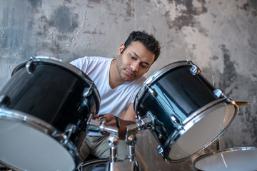 Dark-haired young man in a white tshirt sitting at the drums