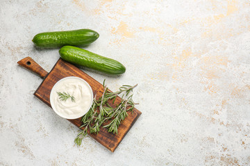 Bowl with tasty sour cream, cucumbers and herbs on table