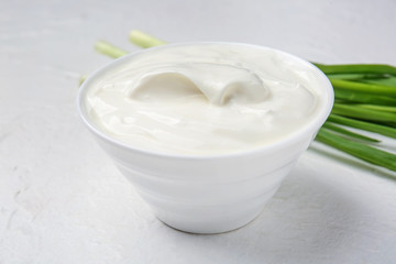 Bowl with tasty sour cream and green onion on white table