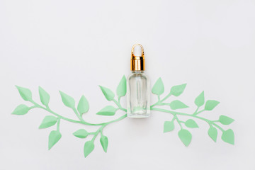 Glass bottle with aroma oil, paper green leaves on white background, aromatherapy concept