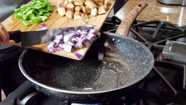 Pushing red onions and peppers into hot pan to cook, potatoes on wooden cutting board
