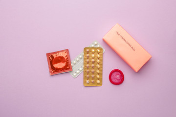 Contraceptive pills and condoms on color background