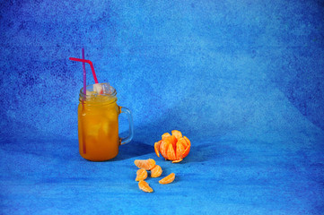 Glass mug of citrus juice with ice with slices of mandarin on a blue background. © Алексей Желтухин