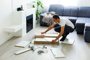 Close-up of young man putting self assembly furniture as they move into your new house.