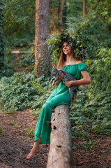 vertical portrait of a barefoot girl in a long green dress on a background of wild forest