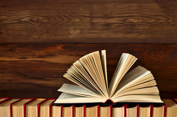 An open book lies on a stack of books on a wooden background.