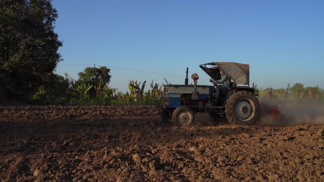 young indian farmer ploughing field with tractor