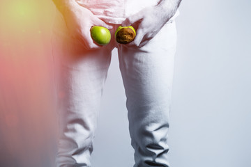 A man at the level of the genitals , holding a ripe and rotten apple. Disease for men. The concept...