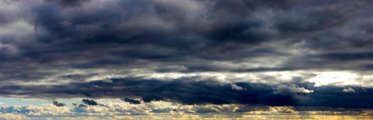 Naklejka na ściany i meble Overcast weather. Ultra wide panoramic background of cloudy sky at sunset. Dark clouds and a glow. Siberia Russia.
