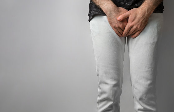 The man in white jeans folded his hands at the level of his genitals. Disease for men. The concept of protection against sexually transmitted infections. Testicular cancer. Copy space