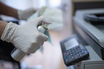 Woman disinfects a printer and a photocopier in the office with a spray disinfectant liquid.