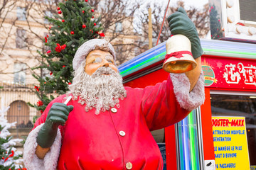 Santa Klaus figurine made of plastic. It's holding a golden bell. Paris Christmas Market (Tuileries gardens), France. Beautiful low angle close up shot at the Fair. Daylight.