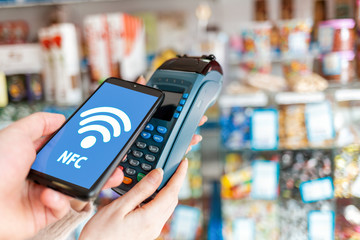 Women's hands are held by a payment terminal and a man pays for a purchase using a smartphone.On...