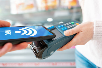 The seller holds a payment terminal, and the man pays for the purchase using a smartphone, online. Hands close up. On the phone screen-wi-fi network. NFC concept, business and banking operations