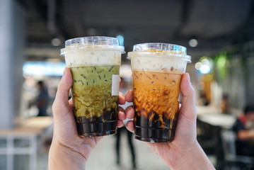 Matcha Green tea and Thai Tea Bubble drinks, man holding a plastic cup of bubble/boba matcha green tea and Thai tea with brown sugar and topped with cheese cream.
