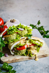 Falafel with fresh vegetables and tahini dressing in pita bread on the board. Healthy vegan food concept.
