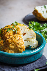Whole baked cauliflower with spices and herbs in blue dish.