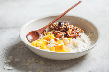 Vegan breakfast with homemade granola, coconut yogurt and mango in white bowl.