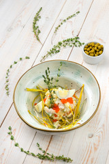 Healthy vegetable salad with eggs, greens, meat and red caviar on beautiful plate, lunch menu of national food restaurant on white wooden background in rustic style