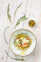 Healthy vegetable salad with eggs, greens, meat and red caviar on beautiful plate, lunch menu of national food restaurant on white wooden background in rustic style, top view